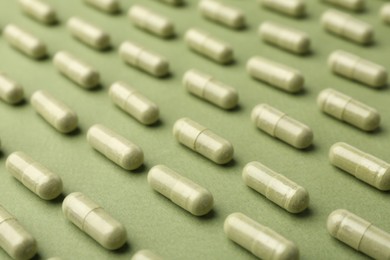 Photo of Many vitamin capsules on olive background, closeup