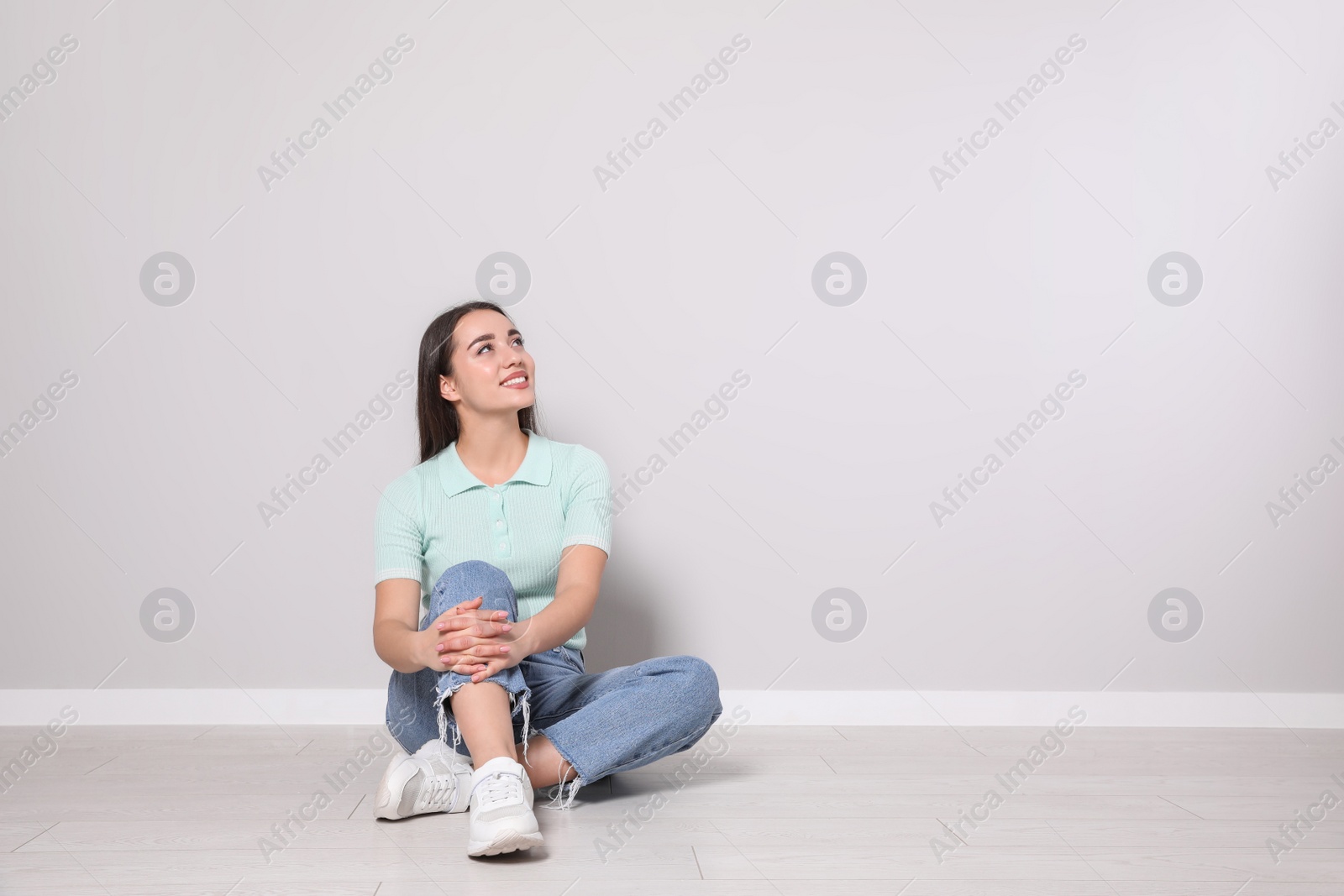 Photo of Young woman sitting on floor near light grey wall indoors. Space for text