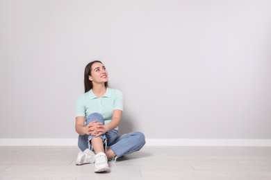 Young woman sitting on floor near light grey wall indoors. Space for text