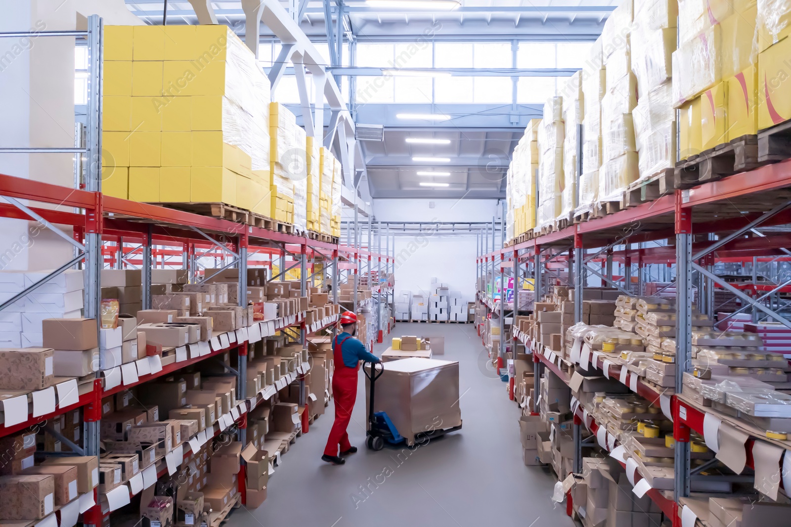 Image of Man in hardhat working with pallet truck at warehouse. Logistics center