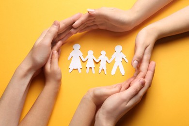 Parents and child protecting paper cutout of family on orange background, top view