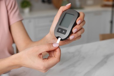 Diabetes. Woman checking blood sugar level with glucometer at white marble table in kitchen, closeup