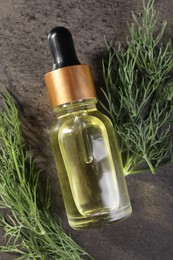 Bottle of essential oil and fresh dill on grey table, top view
