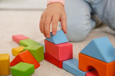Photo of Cute little girl playing with colorful building blocks on floor, closeup