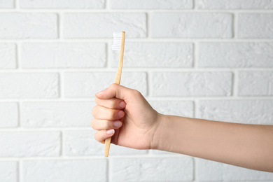 Photo of Woman holding bamboo toothbrush against white brick wall, closeup