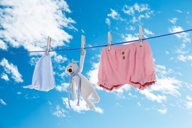 Image of Baby clothes and crochet toy drying on washing line against sky