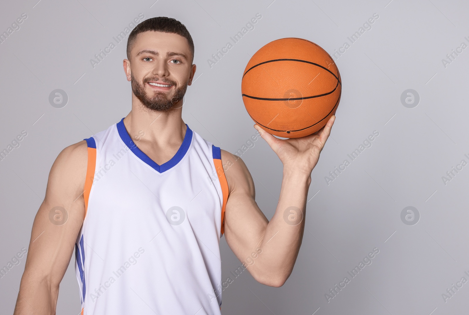 Photo of Athletic young man with basketball ball on light grey background. Space for text