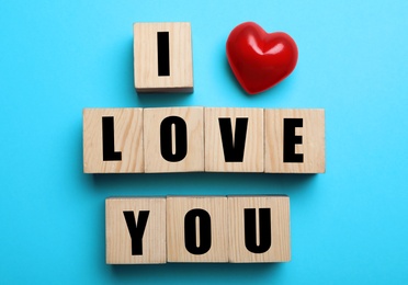 Cubes with words I Love You and red heart on light blue background, flat lay