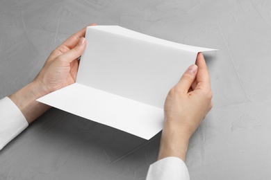 Photo of Young woman holding blank brochure at grey table, closeup. Mock up for design