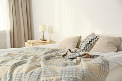 Photo of Bed with pillows and plaid near light wall. Cozy interior design