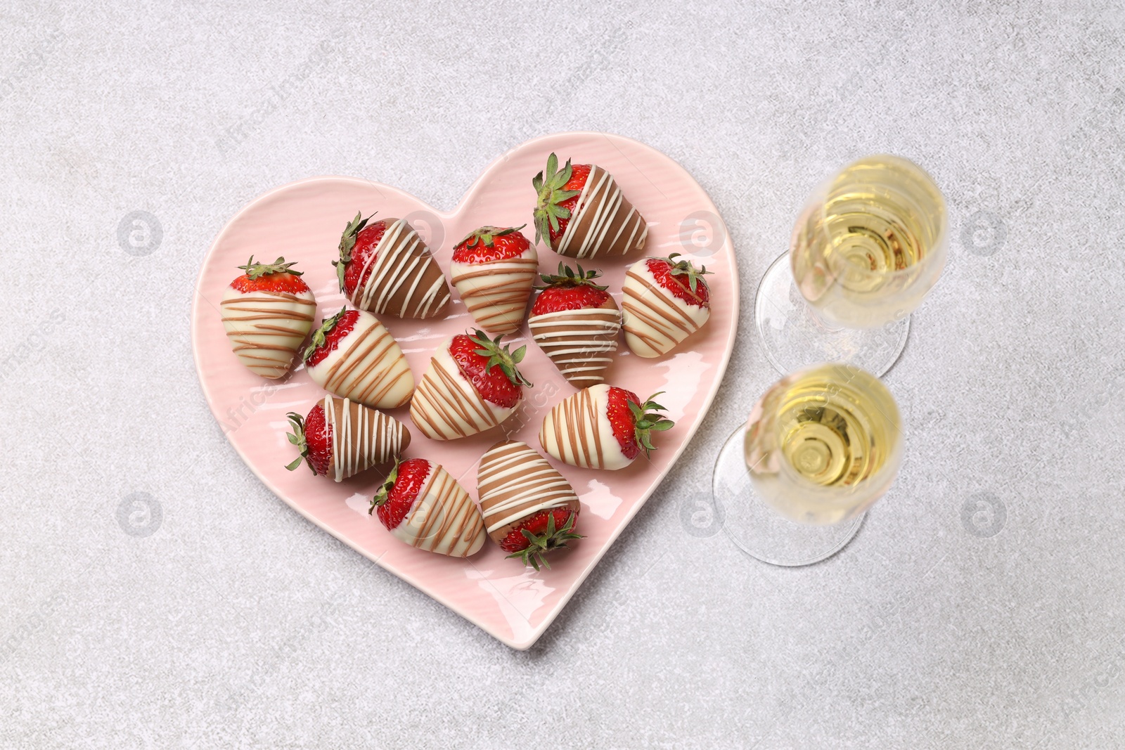 Photo of Heart shaped plate with delicious chocolate covered strawberries and sparkling wine on light table, flat lay