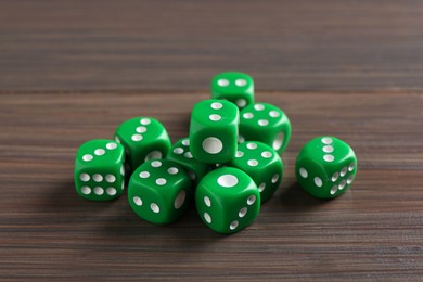 Photo of Many green game dices on wooden table, closeup