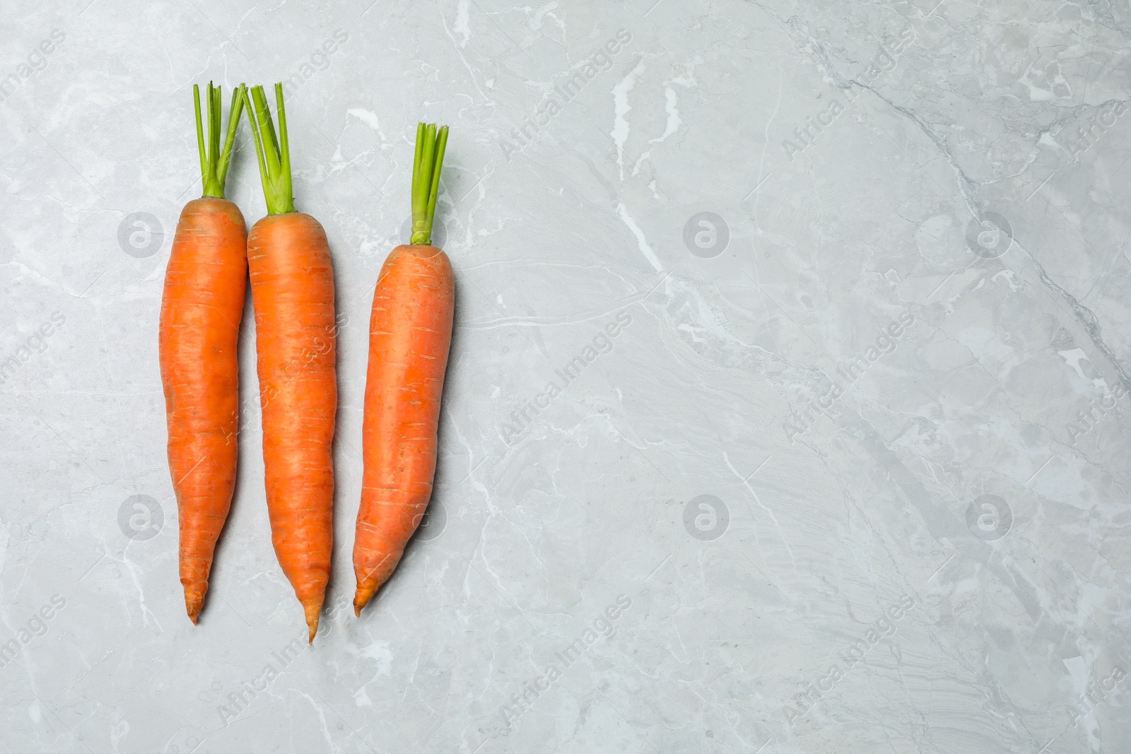 Photo of Fresh ripe juicy carrots on light grey marble table, flat lay. Space for text