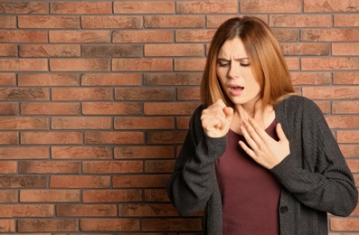 Woman suffering from cough near brick wall. Space for text