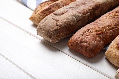 Photo of Different tasty baguettes on white wooden table, closeup. Space for text