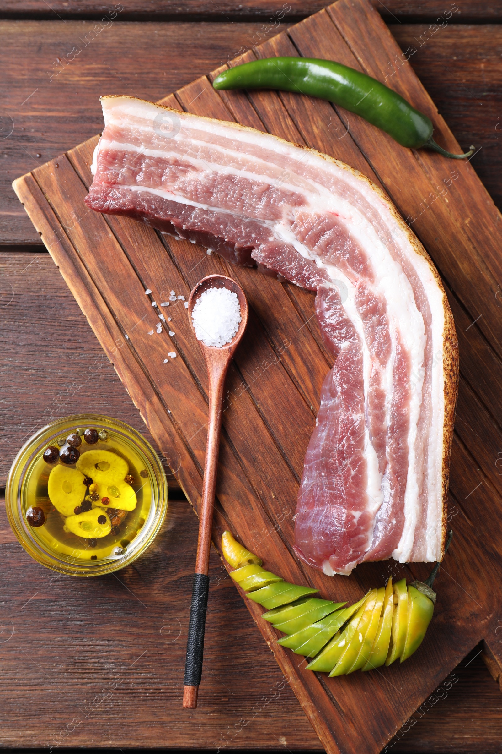 Photo of Piece of raw pork belly, green chili pepper and oil with spices on wooden table, top view