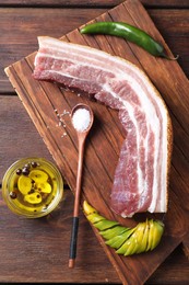 Piece of raw pork belly, green chili pepper and oil with spices on wooden table, top view