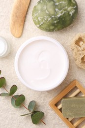 Photo of Flat lay composition with moisturizing cream in open jar and other body care products on light textured table