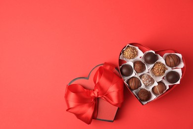 Photo of Heart shaped box with delicious chocolate candies on red table, flat lay. Space for text