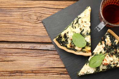 Pieces of delicious homemade spinach quiche and tea on wooden table, flat lay. Space for text