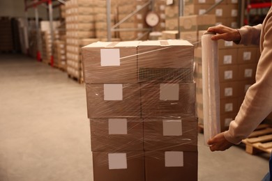 Photo of Worker wrapping boxes in stretch film at warehouse, closeup