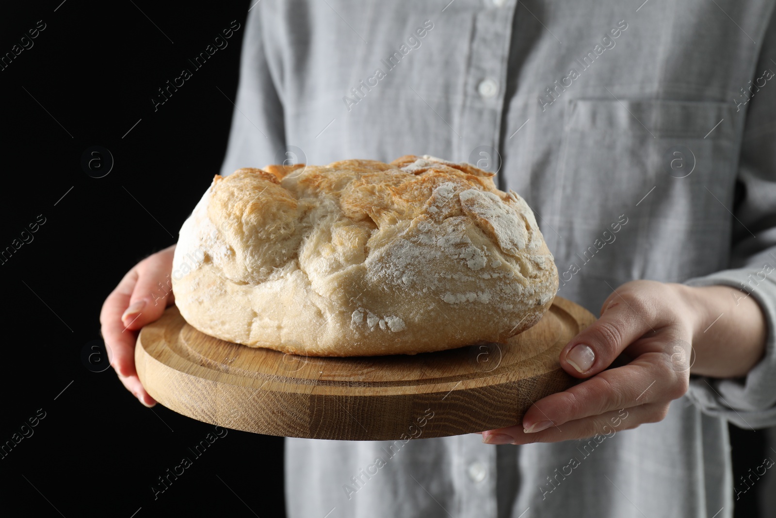 Photo of Woman holding freshly baked bread on black background, closeup