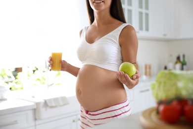 Young pregnant woman with apple and glass of juice in kitchen, closeup. Taking care of baby health