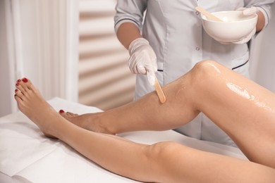 Photo of Professional cosmetologist applying gel on client's leg before laser epilation procedure in salon, closeup
