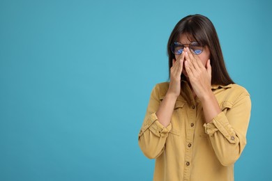 Resentful woman covering face with hands on light blue background, space for text