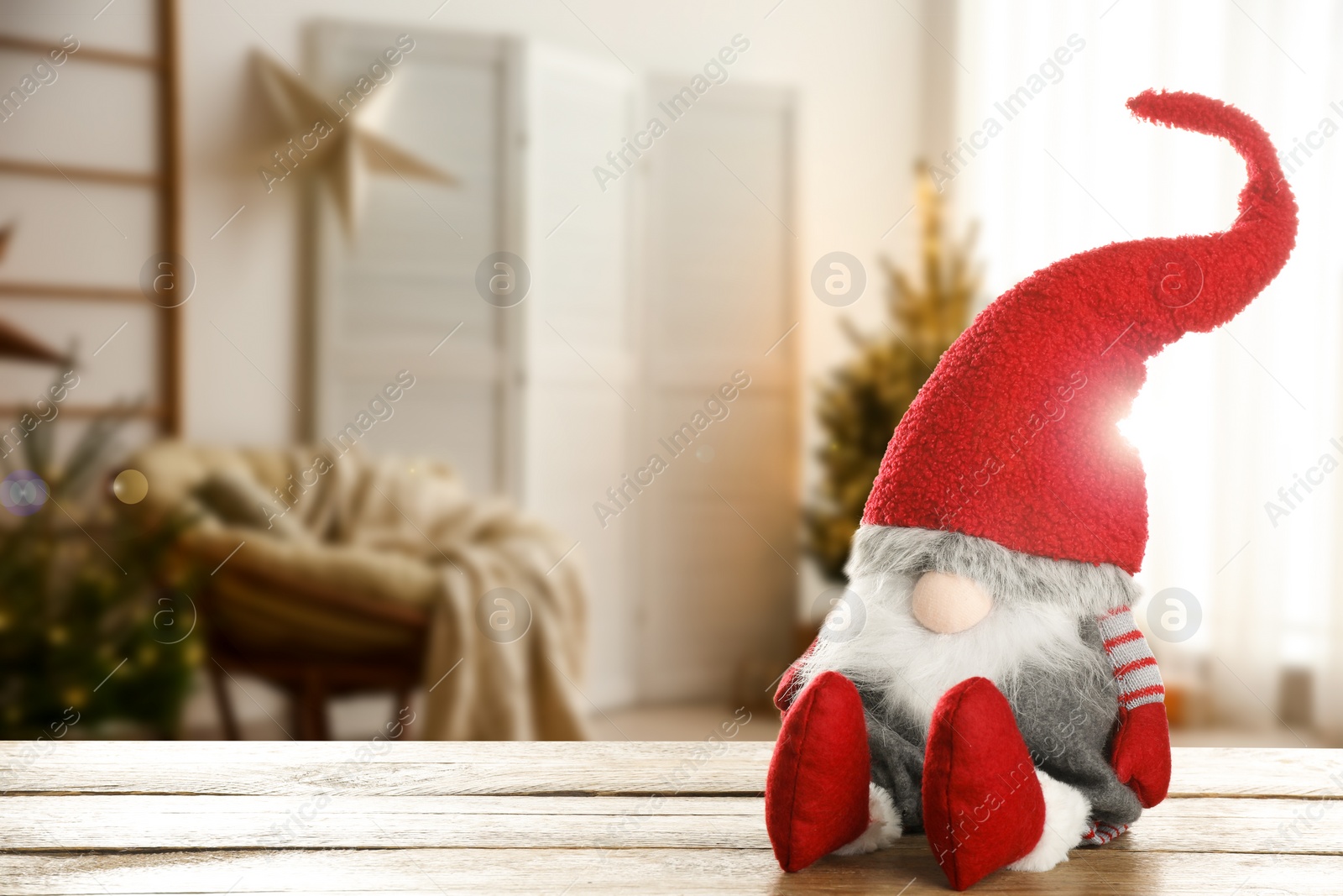 Image of Funny Christmas gnome on wooden table in room with festive decorations. Space for text