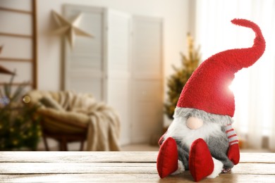 Image of Funny Christmas gnome on wooden table in room with festive decorations. Space for text