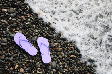 Photo of Stylish flip lops on pebble beach near sea. Space for text