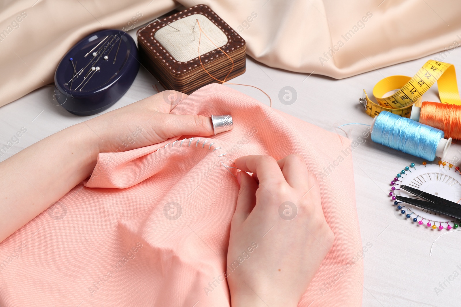 Photo of Woman with sewing needle and thread embroidering on cloth at white wooden table, closeup