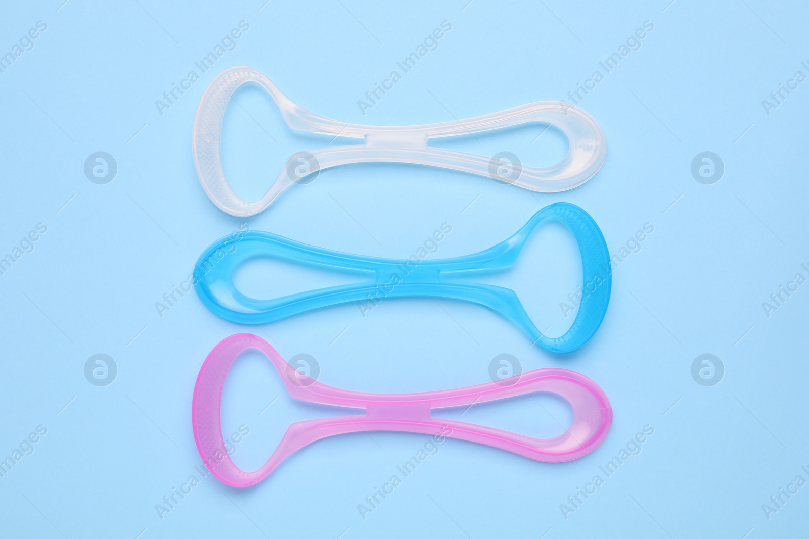 Photo of Colorful tongue cleaners on light blue background, flat lay