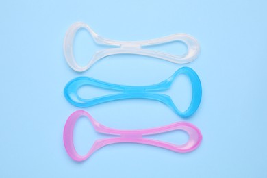 Photo of Colorful tongue cleaners on light blue background, flat lay