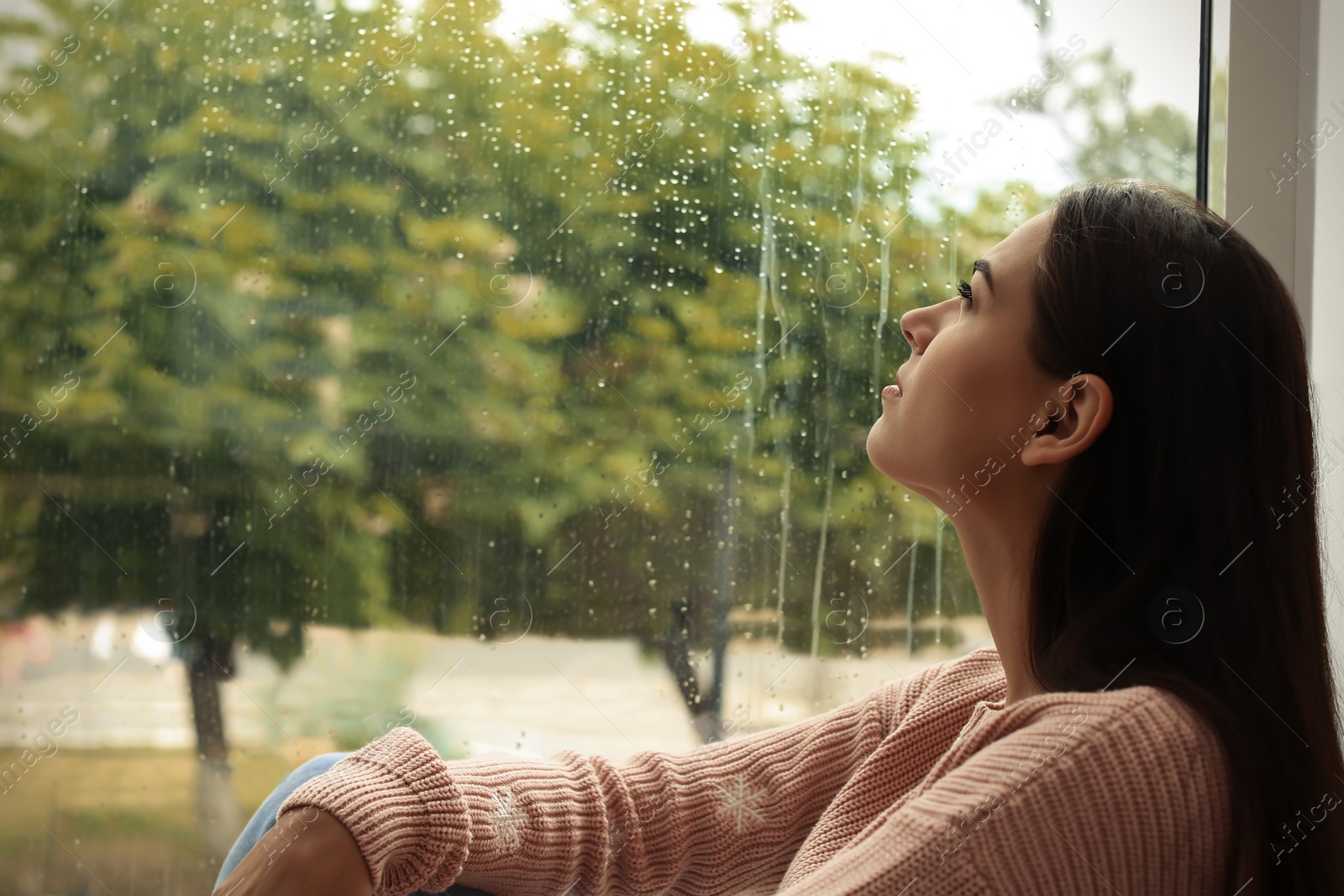 Photo of Young sad woman sitting near window at home