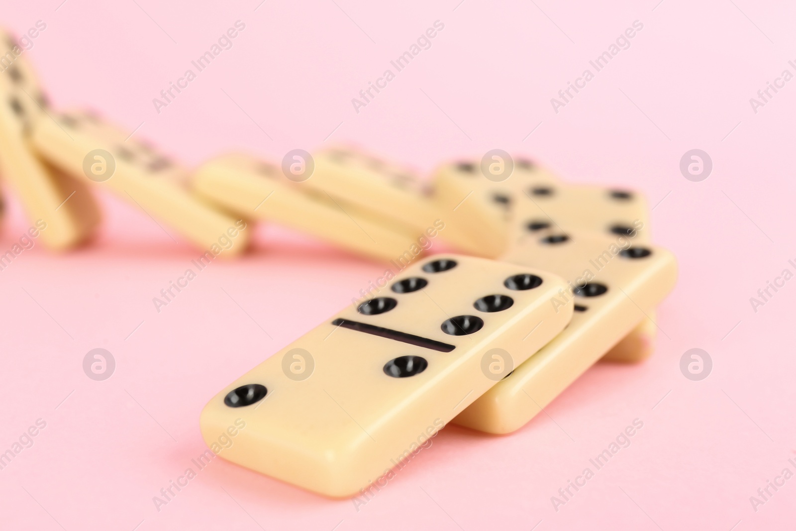 Photo of White domino tiles falling on pink background, closeup. Space for text