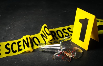 Photo of Broken bottle, yellow tape and crime scene marker on black table, closeup