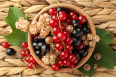 Different fresh ripe currants and green leaves on wicker surface, top view