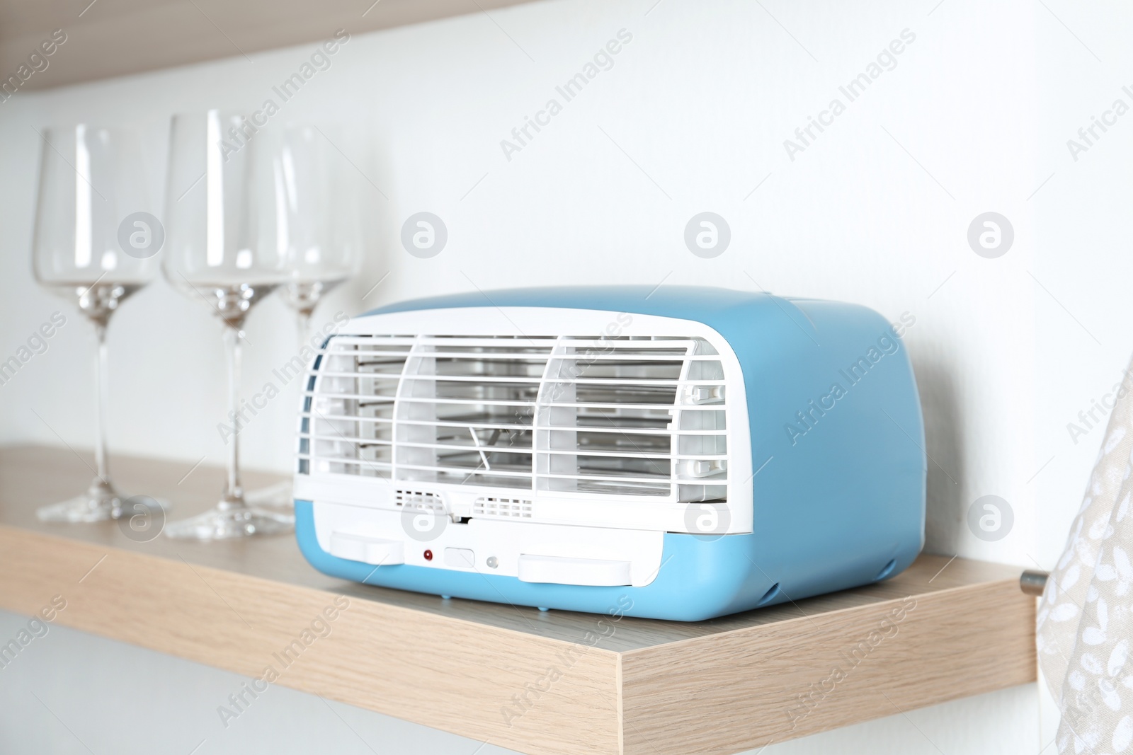 Photo of Modern air purifier and glasses on wooden shelf in kitchen