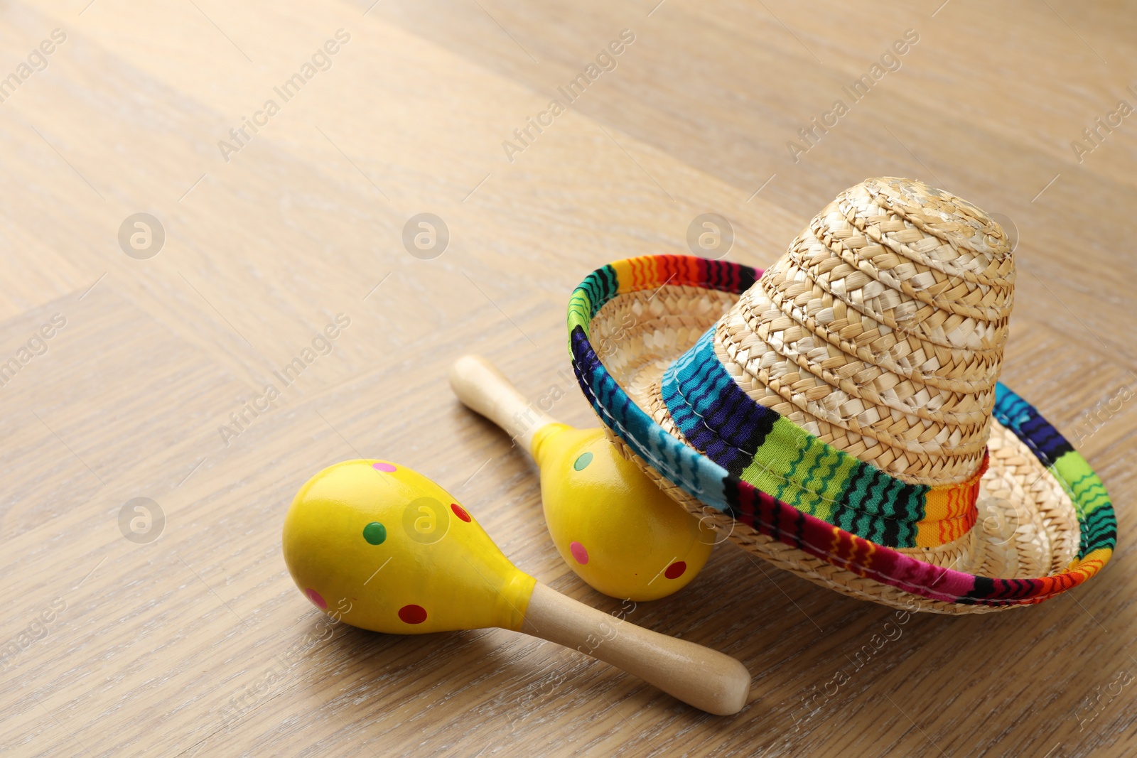 Photo of Mexican sombrero hat and maracas on wooden table. Space for text