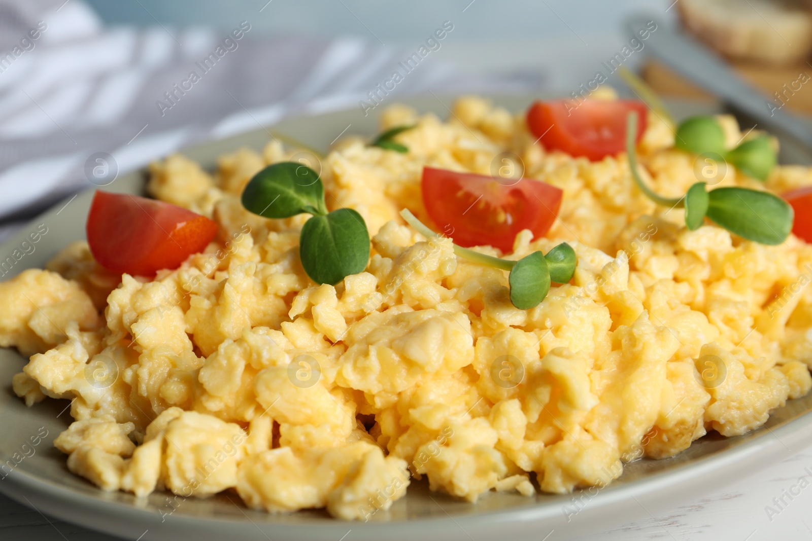 Photo of Tasty scrambled eggs with sprouts and cherry tomato on grey plate, closeup