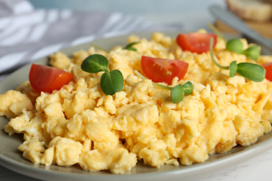 Photo of Tasty scrambled eggs with sprouts and cherry tomato on grey plate, closeup