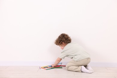 Photo of Little boy with colorful pencils near white wall indoors. Space for text