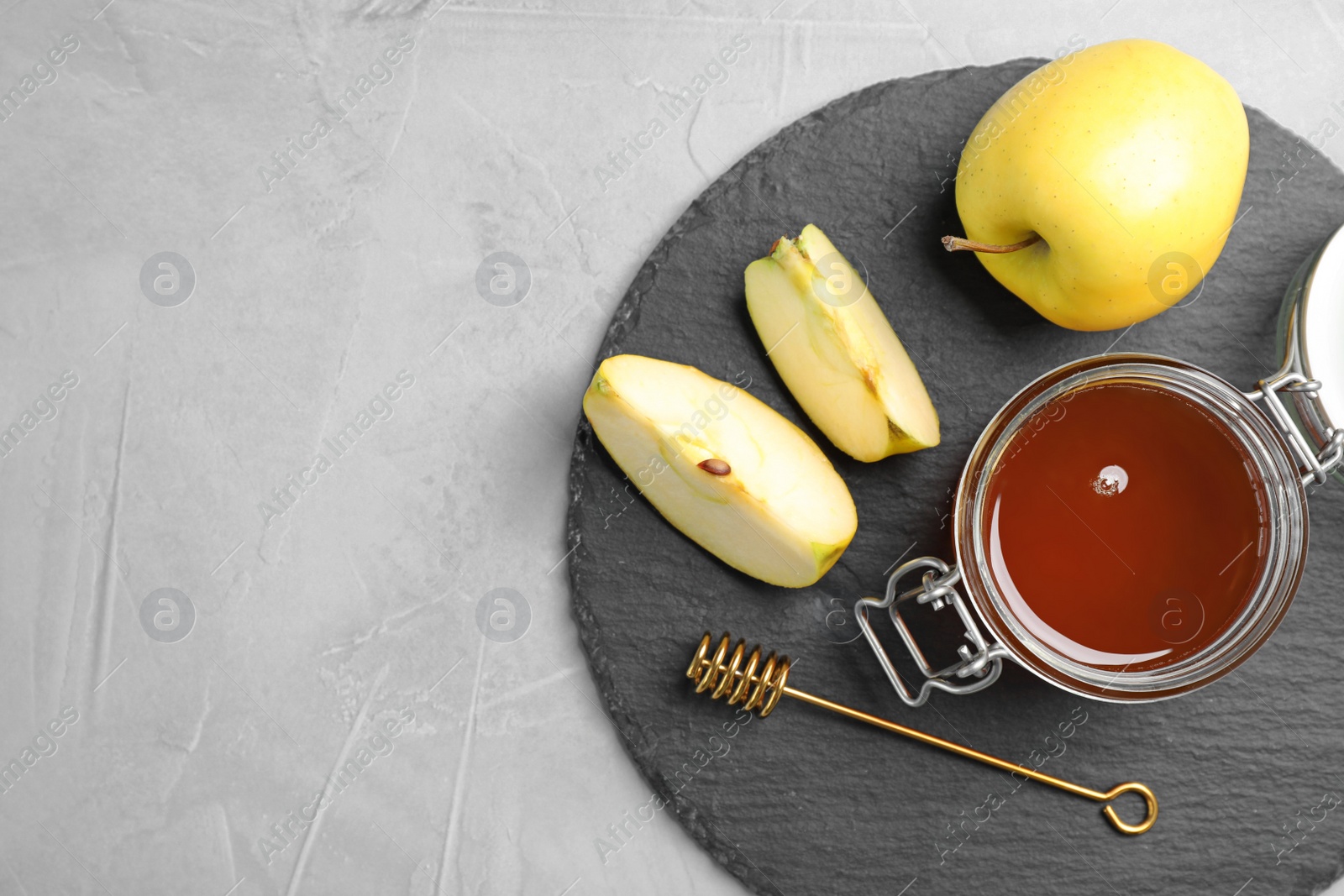 Photo of Slate plate with jar of honey, apples and dipper on gray background, flat lay