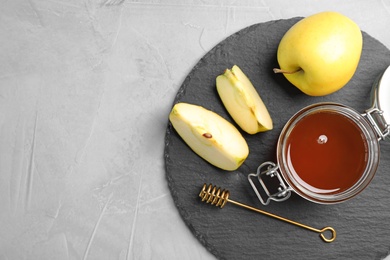 Slate plate with jar of honey, apples and dipper on gray background, flat lay