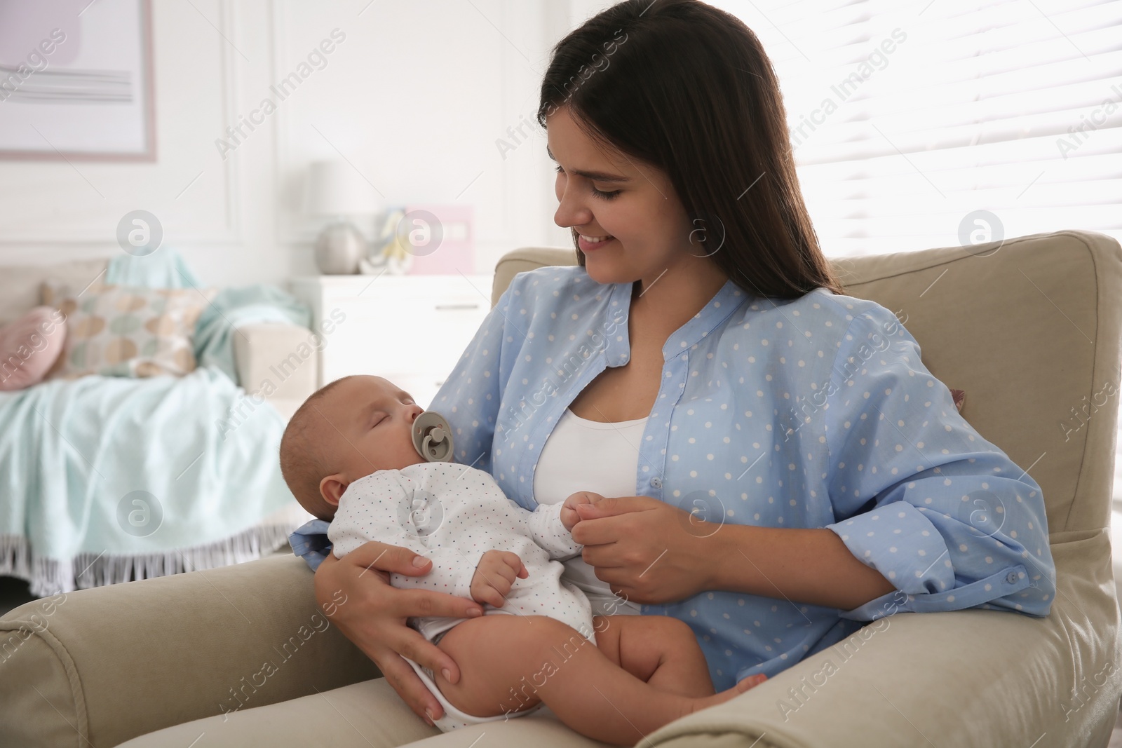 Photo of Happy mother holding her cute sleeping baby with pacifier at home