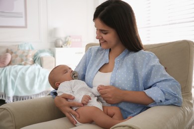 Happy mother holding her cute sleeping baby with pacifier at home