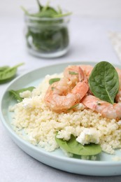 Photo of Plate of delicious couscous with shrimps and spinach on white table, closeup