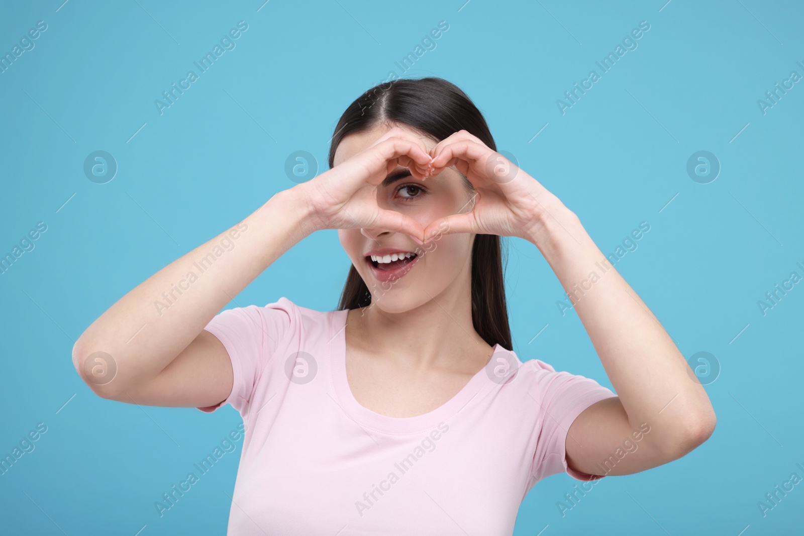 Photo of Beautiful young woman making heart with hands on light blue background